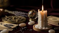 Mystical fortune telling setup with burning candle, tarot cards, crystal ball and magical accessories on dark wooden table for divination practices.