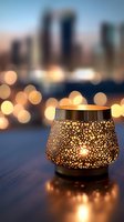 Ornate metal candle holder with glowing floral pattern against blurred city skyline and bokeh lights at dusk, creating romantic ambiance on wooden surface.