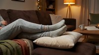 Cozy evening at home with person in gray wool socks relaxing on brown leather sofa with warm lighting and comfortable interior design atmosphere.