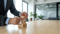 Professional businessman stacking wooden blocks with customer service icons on office desk, representing business growth and client satisfaction strategy.