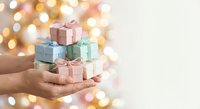 Hands holding stack of pastel gift boxes with ribbons against warm bokeh lights background for holiday celebrations and special occasions.