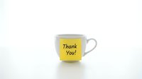 White ceramic coffee cup with a yellow sticky note saying Thank You, placed on a white surface, conveying gratitude and appreciation.