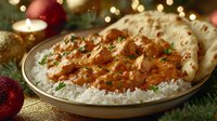 Creamy butter chicken curry served with steamed basmati rice and naan bread garnished with fresh herbs against festive Christmas decorations and lights.