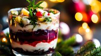 Festive layered dessert with cream, berries and chocolate crumbs in glass, decorated with mint leaves against blurred Christmas lights background.