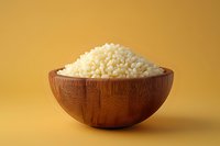 Uncooked white rice grains in wooden bowl against vibrant yellow background, minimalist food photography composition for culinary and healthy eating concepts.