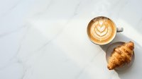 Overhead view of cappuccino with latte art and fresh croissant on marble surface, ideal for cafe, bakery, and breakfast-themed designs.
