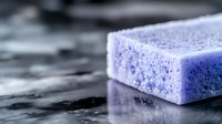 Macro shot of purple soap bar with foam texture on dark wet surface showing bubbles and moisture details, highlighting cleaning and hygiene concept.