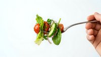 Fresh mixed salad on fork with lettuce, tomatoes and cucumber held by hand against white background for healthy eating concepts.