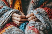 Female hands gently holding soft knitted multicolored wool blanket with cozy pattern texture, creating warm and comfortable atmosphere for winter season relaxation.
