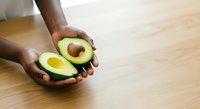 Fresh avocado halves with pit held in hands over wooden surface, showcasing healthy organic produce for cooking, nutrition, and food styling projects.