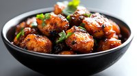 Glazed meatballs with sesame seeds and fresh herbs in black bowl, savory comfort food dish with glossy sauce perfect for restaurant menu photography.
