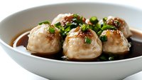 Asian pork meatballs in savory soy glaze with fresh herbs served in white ceramic bowl for restaurant menu and cooking content.