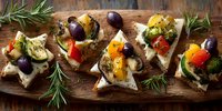 Mediterranean bruschetta appetizers with roasted vegetables, olives, and herbs on rustic wooden board.