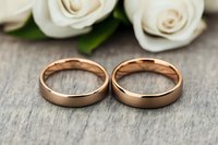 Two elegant rose gold wedding rings on rustic wood surface with white roses, symbolizing eternal love and commitment for marriage ceremonies.