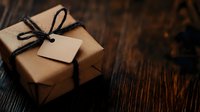 Rustic kraft paper gift box with black twine bow and blank tag on dark wooden background, moody atmospheric holiday composition for greeting cards.