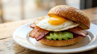 Gourmet breakfast burger with fried egg, crispy bacon and fresh lettuce on sesame seed bun served on white plate for restaurant menu and food photography.