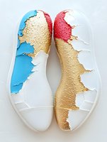 Creative white leather ballet flats decorated with abstract gold, blue and pink paint splatter design showing artistic wear pattern on dance shoes.