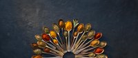Colorful spices and seasonings arranged in wooden spoons on dark slate background for culinary cooking and food preparation projects.