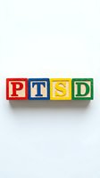 Colorful wooden toy blocks spelling PTSD in red, blue, yellow, and green on white background. Mental health awareness and trauma education concept.