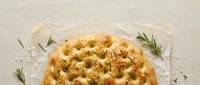 Homemade focaccia bread with rosemary herbs and olive oil on parchment paper, traditional Italian flatbread perfect for cooking and food photography.