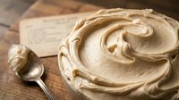 Creamy peanut butter spread in bowl with spoon on wooden surface, ready for cooking, baking, or sandwich preparation.