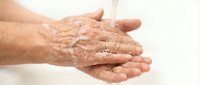 Elderly woman washing hands under running water with soap, hygiene and health care concept, isolated on light background.
