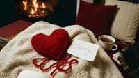 Knitted red heart with sorry note on cozy blanket near fireplace, tea cup and cat, romantic apology concept.