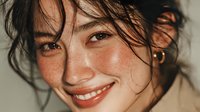 Young Asian woman with wet hair and natural makeup smiling warmly at camera. Fresh dewy skin with freckles and messy hair strands. Beauty skincare lifestyle portrait.