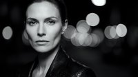 Confident young Caucasian woman with intense gaze in black and white portrait against blurred city lights bokeh background for commercial use.