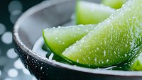 Fresh lime wedges with water drops in dark bowl against blurred background, macro shot highlighting citrus texture and juicy pulp for food and beverage styling.