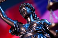 Bronze statue of Lady Justice holding scales and sword against dramatic red and blue background, symbol of law and justice system, close-up view with metallic finish.