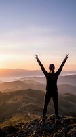 Woman hiker celebrating success with raised arms on mountain peak at sunrise overlooking layered hills and valleys in golden light.