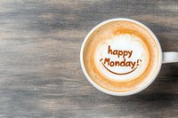 Cappuccino foam art with happy Monday message and smiley face drawn in coffee on wooden table background, positive morning motivation concept.