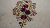 Embroidered red roses with golden leaves on beige linen fabric. Traditional floral needlework design with decorative border elements for textile crafts.