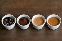 Four white cups showing coffee evolution from beans to ground coffee to espresso and latte on rustic wooden table. Perfect for coffee shop menu.