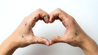 Hands covered in colorful paint spots forming a heart shape, symbolizing love for art and creativity, isolated on white background.
