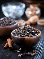 Raw cacao nibs in wooden bowl with cinnamon sticks on dark rustic table, selective focus on organic superfood ingredients for healthy eating.