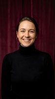 Professional Caucasian woman in black turtleneck smiling confidently against burgundy curtain backdrop for business presentations and corporate materials.
