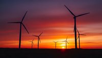 Wind turbines silhouetted against dramatic sunset sky with orange and purple colors. Renewable energy concept for sustainable power generation and clean technology.