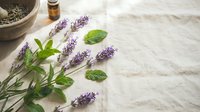 Fresh lavender sprigs with green leaves arranged on rustic wooden surface alongside mortar pestle and essential oil bottle for aromatherapy and natural wellness.
