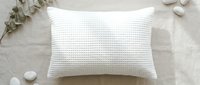 White textured pillow on neutral background with decorative stones and dried botanicals, suitable for home decor and bedding product photography.