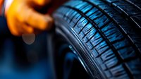 Close-up view of black rubber tire tread pattern with dramatic lighting and orange glow in background, showing detailed texture and grooves of automotive wheel.