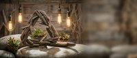 Rustic wooden basket filled with fresh green vegetables on stone surface with warm Edison bulb lighting creating cozy farmhouse kitchen atmosphere.