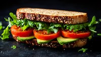 Fresh vegetable sandwich with tomatoes, cucumber, arugula on whole grain bread against dark background, close up view of healthy lunch meal preparation.