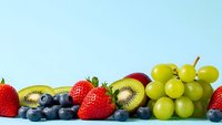 Fresh mixed fruits arrangement with strawberries, blueberries, kiwi and green grapes on light blue background for healthy eating and nutrition concepts.