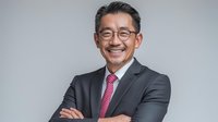 Confident Asian businessman in gray suit with pink tie smiling with arms crossed against neutral background, portraying leadership and success.