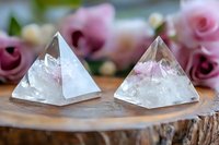 Clear quartz crystal pyramids with pink inclusions on rustic wooden surface, surrounded by soft pink roses creating mystical healing atmosphere.
