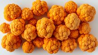 Fresh orange cauliflower florets scattered on white background, organic healthy vegetable pattern, raw food ingredient for cooking and nutrition.