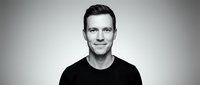Portrait of a young adult male with fair complexion and dark hair, wearing a black casual t-shirt against neutral background for professional headshots and corporate use.