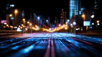 Futuristic city nightscape with glowing audio equalizer bars rising from illuminated streets, creating dynamic visualization with bokeh lights and motion blur effect.